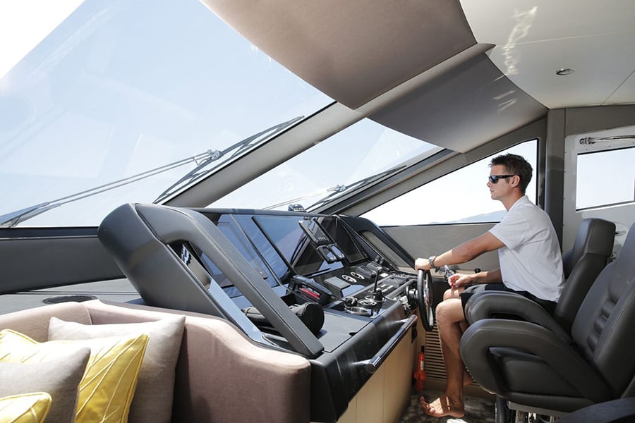 luxury yachts - man in cockpit of yacht holding the helm