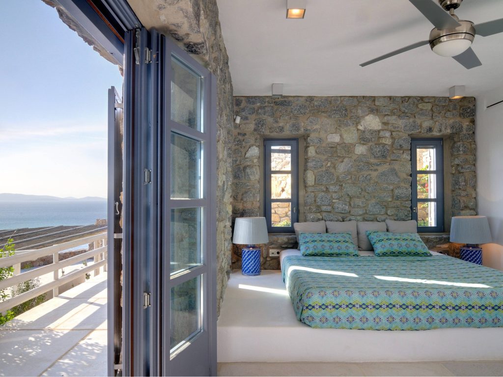luxury villas - bedroom with walls of stone and open door to the balcony